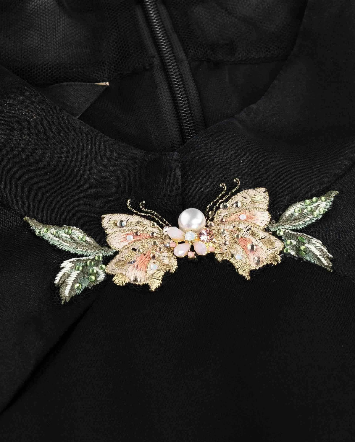 A pale floral accent with leaf details sits below the upright neckline against black.