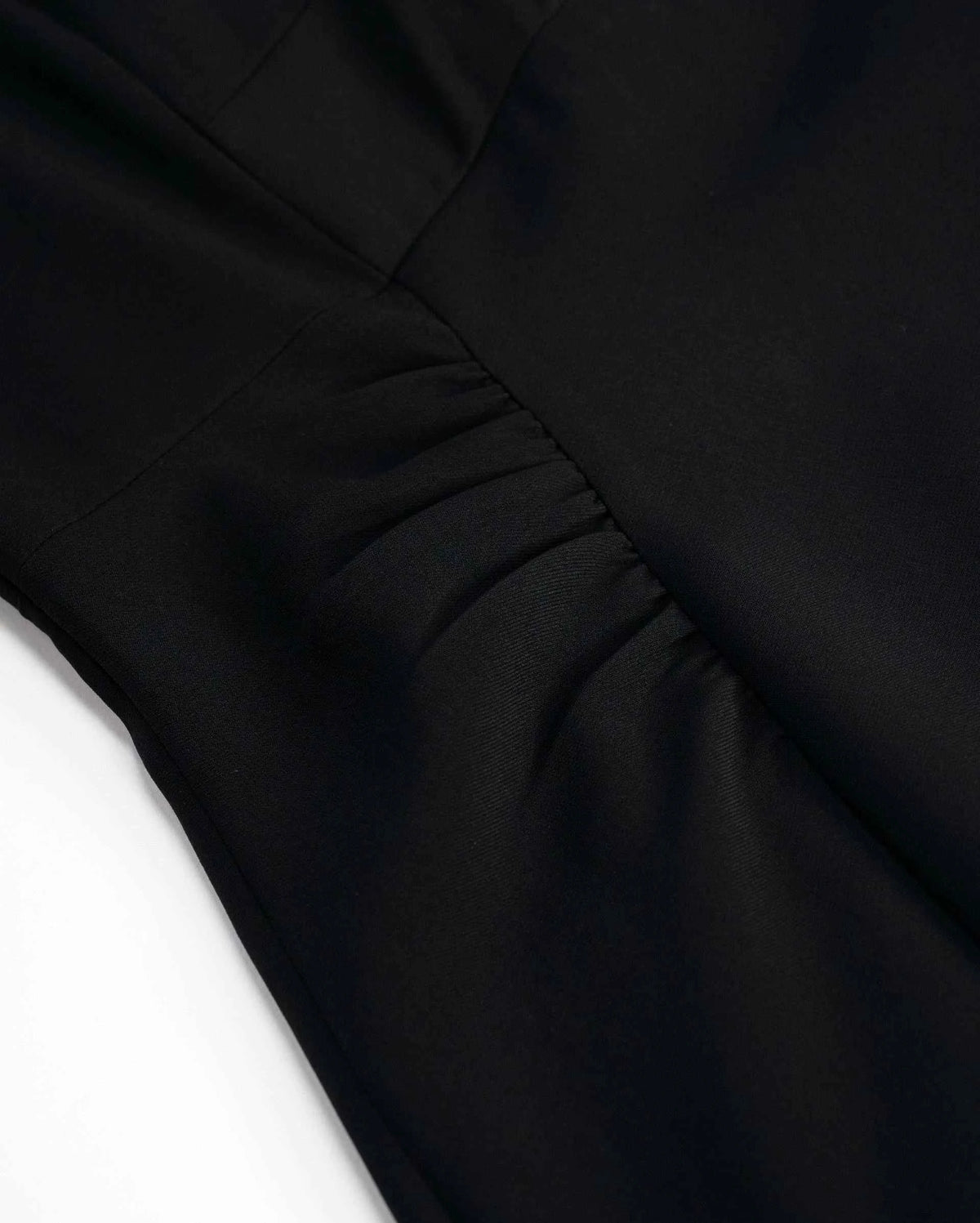 The black fabric draws into close gathers through the body, creating small shifts of light along each fold.