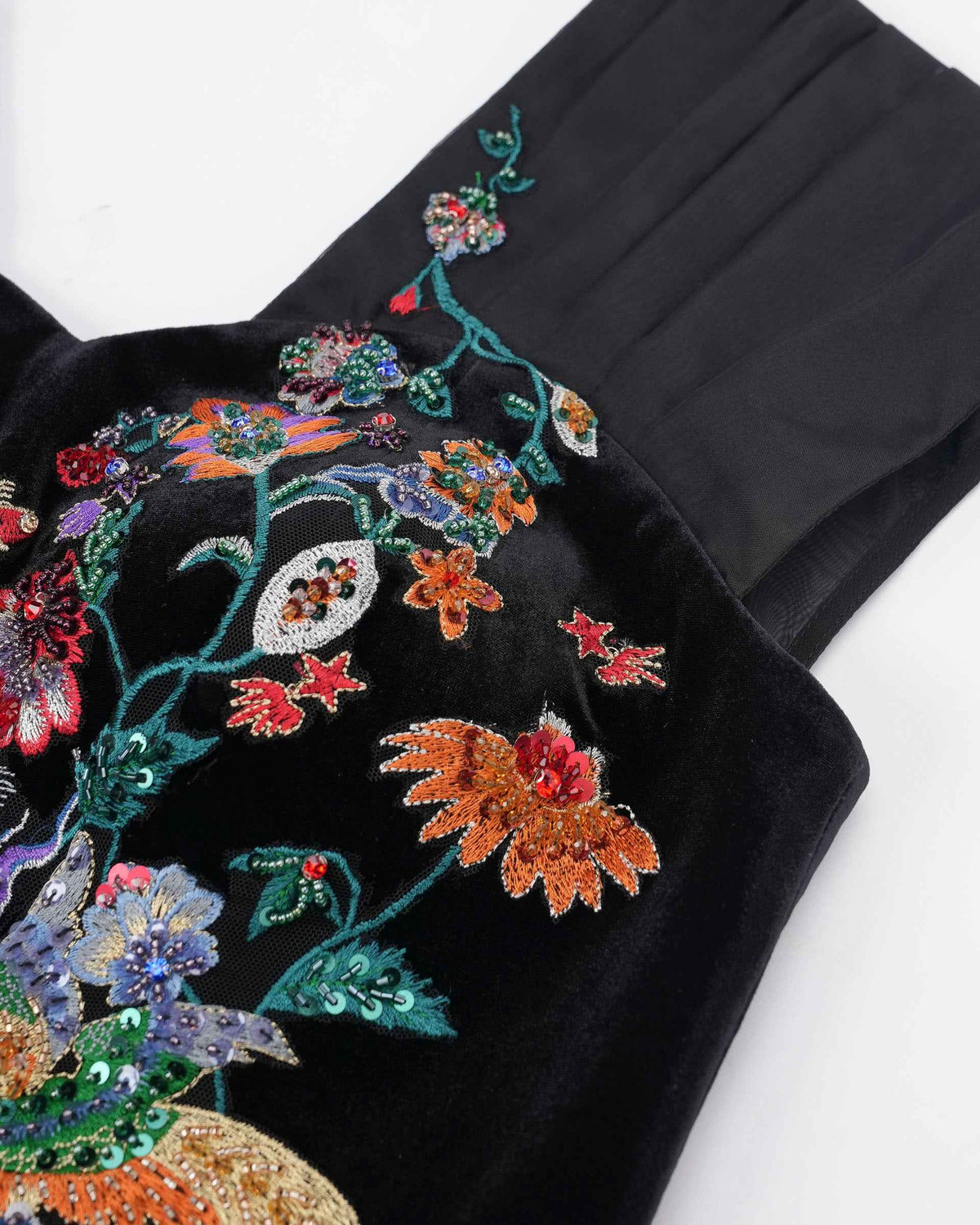 Broad pleats rise at the shoulder beside the embroidered bodice, creating a distinct frame for the neckline.