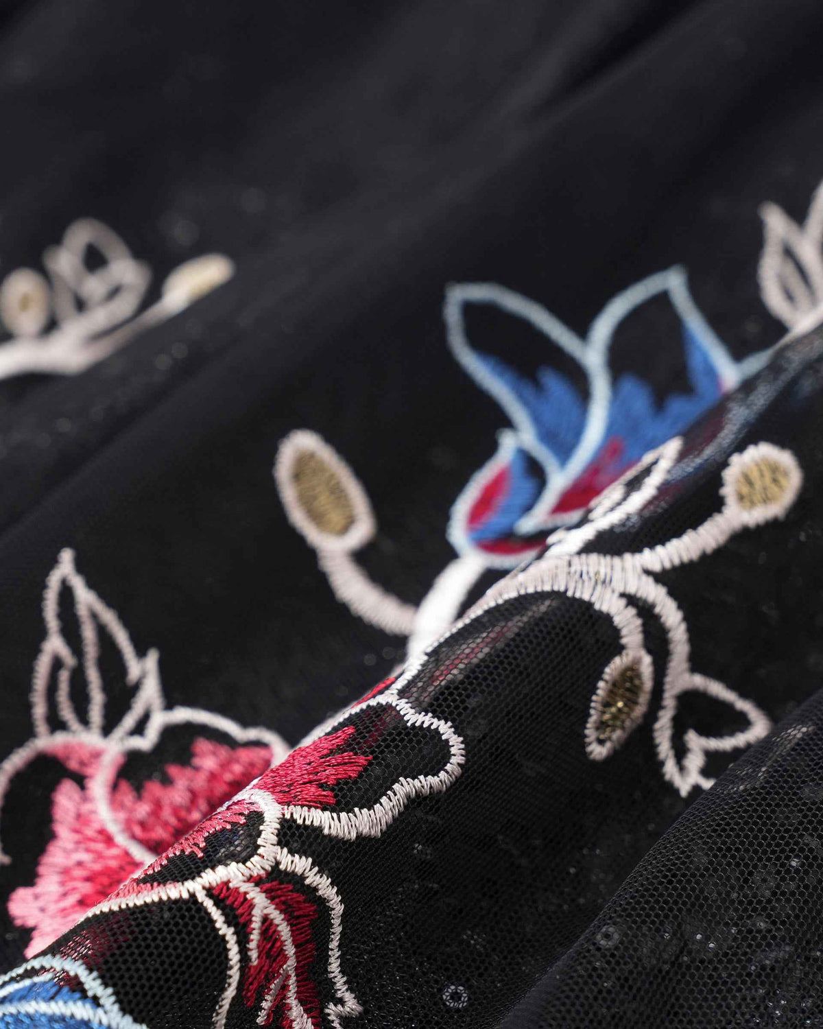 Blue and pink threads outline petals beside pale stems on the black fabric.