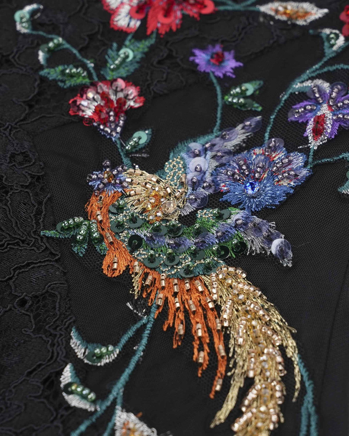 A colourful bird with trailing feathers appears among the floral embroidery.
