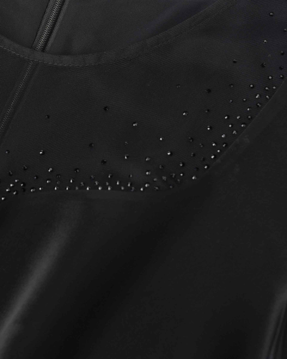 Small dark embellishments trace a curved line near the neckline, catching light subtly against black.