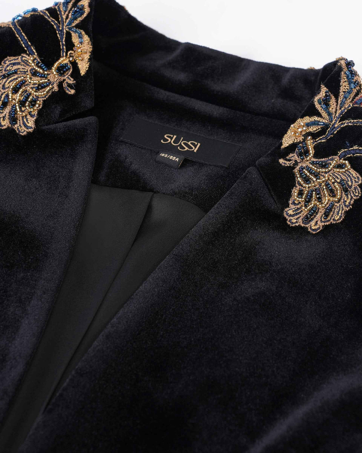 Floral embroidery follows the blazer's neckline in gold, blue, and pale tones.