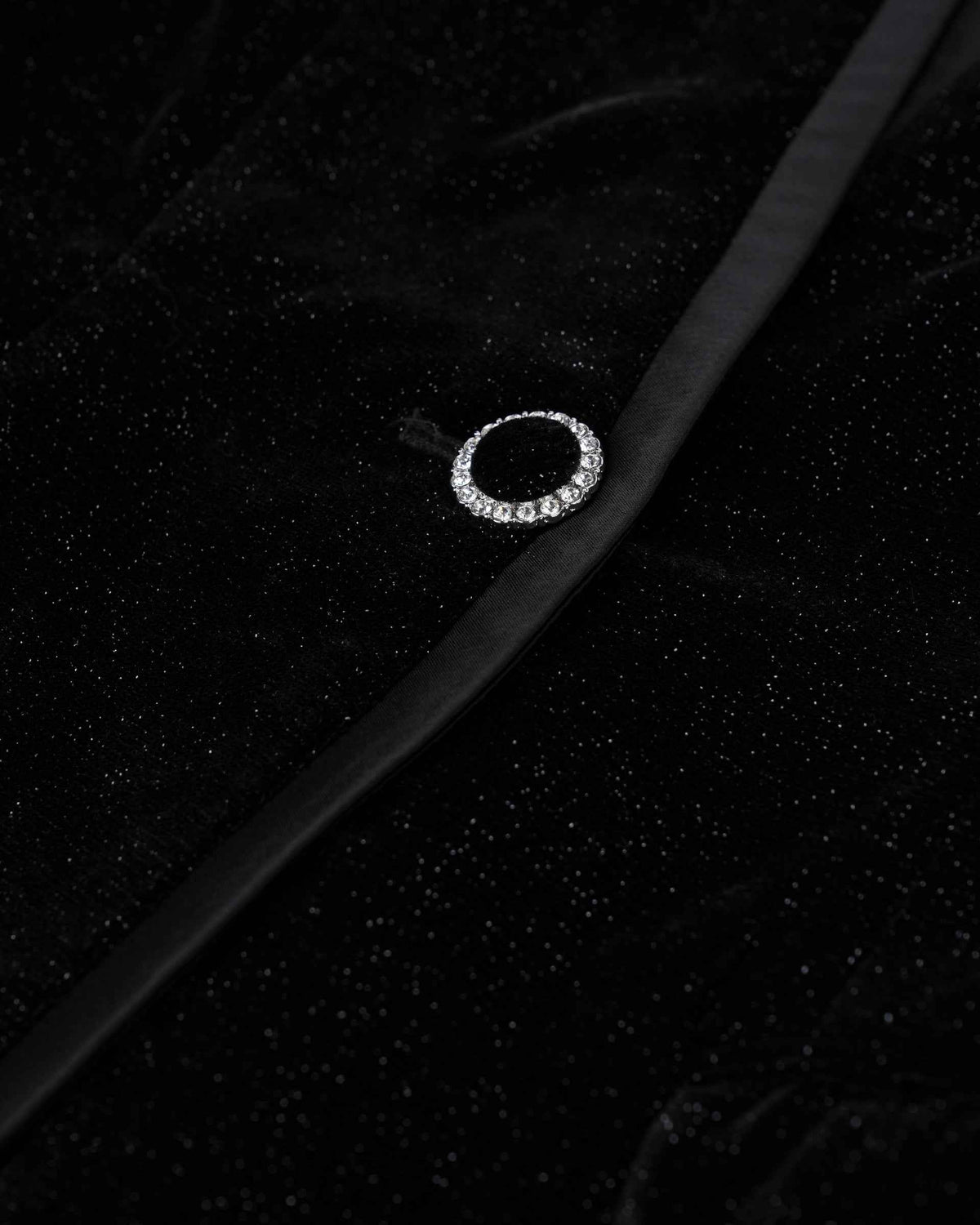 A circular, light-catching fastening sits beside the blazer's dark front edge.