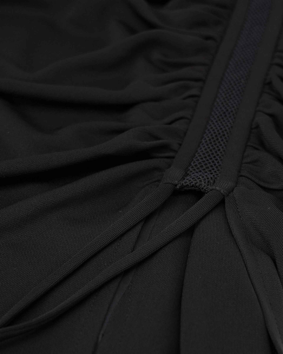 Closely spaced folds gather along a narrow strip of dark fabric, creating a repeated pattern of light and shadow.