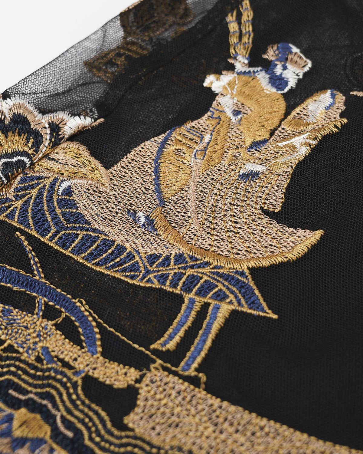 The close-up reveals a richly embroidered figure framed by flowing lines and decorative shapes.