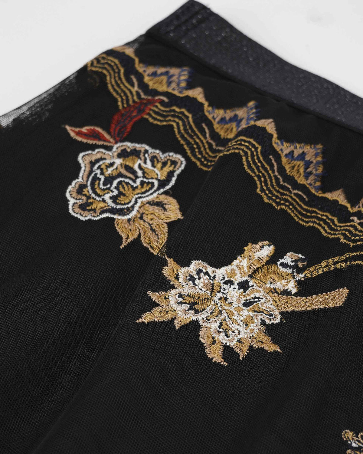 Embroidered flowers and flowing gold-toned lines sit on the black mesh near the waist.
