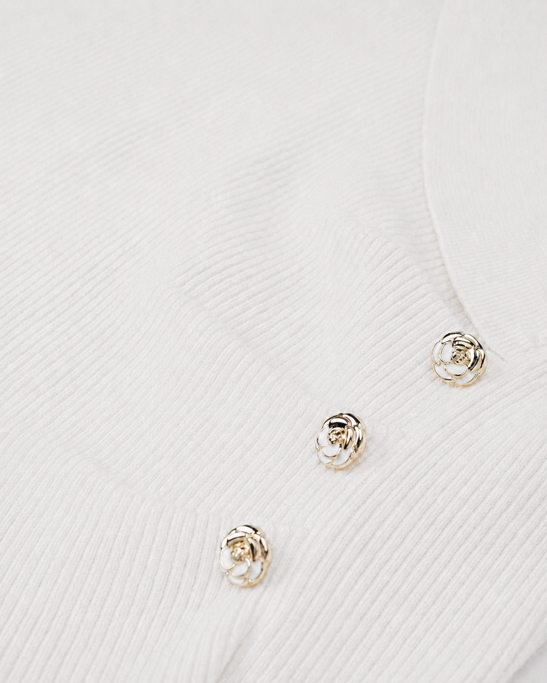Small gold-toned buttons sit along the ivory knit, adding a concentrated decorative accent.